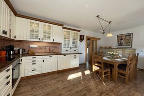 Eine Küche mit weißen Schränken, einer Holzausziehtafel und einem Essbereich mit Tisch und Stühlen.