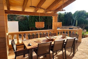 Eine Außenpatio mit einem Holztisch und Stühlen, hängenden Lampen und einer Steinbalustrade.