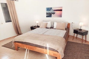 A bedroom with a bed, two bedside tables, a window with curtains, a wall-mounted picture, and a rug. - Holiday home with 2 bedrooms (Cala Llombards)
