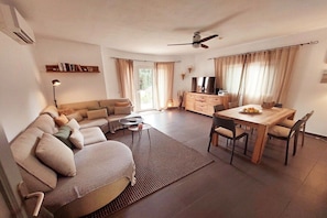 A modern living room with a sofa, dining table, and a ceiling fan. - Holiday home with 2 bedrooms (Cala Llombards)