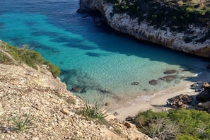 Eine Küstenlandschaft mit klarem türkisblauem Wasser, felsigem Gelände und spärlicher Vegetation.