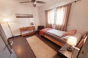 Ein Schlafzimmer mit einem Bett, einem Nachttisch, einer Lampe und einem Deckenventilator.