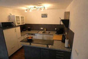 A compact kitchen with a microwave, a sink, a clock, and a bowl of fruit on the counter. - Holiday home in houses with swimming pool (Häusern)