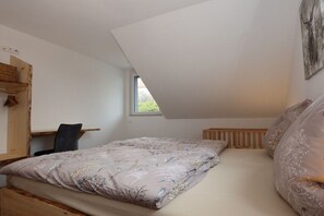 A bedroom with a sloped ceiling, a bed with floral bedding, a chair, a wooden shelf, and a window. - Holiday home in houses with swimming pool (Häusern)