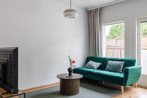 Ein Wohnzimmer mit einem grünen Sofa, einem runden Couchtisch und einem Fernseher auf einem Lowboard.