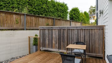 Une terrasse en bois avec une table et une chaise, entourée d’une clôture en bois et d’une haie.