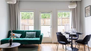 A modern living room with a green sofa, a round table with chairs, and large windows with curtains.