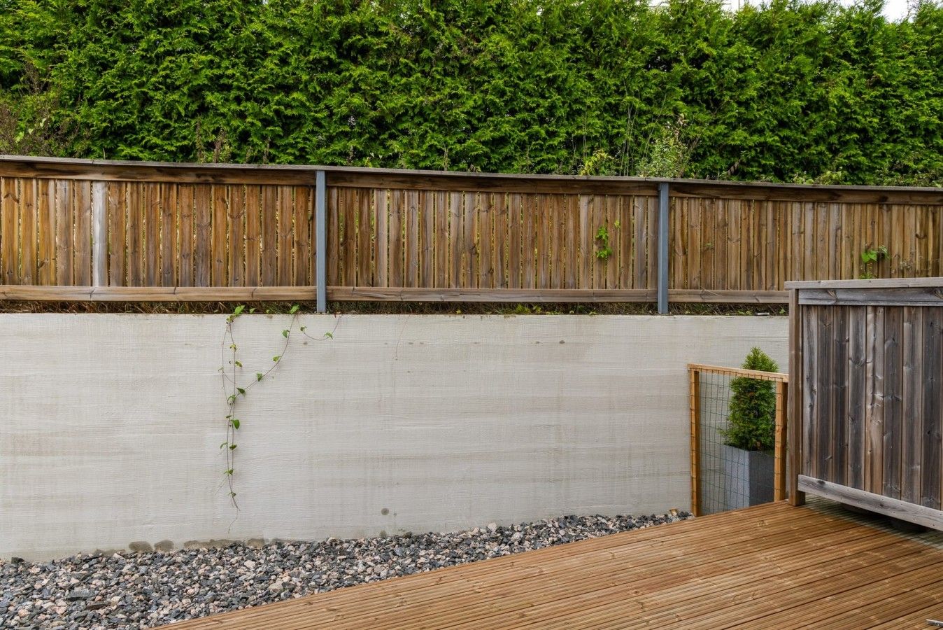 Eine Holzterrasse mit einer Betonmauer und einem Metallzaun.