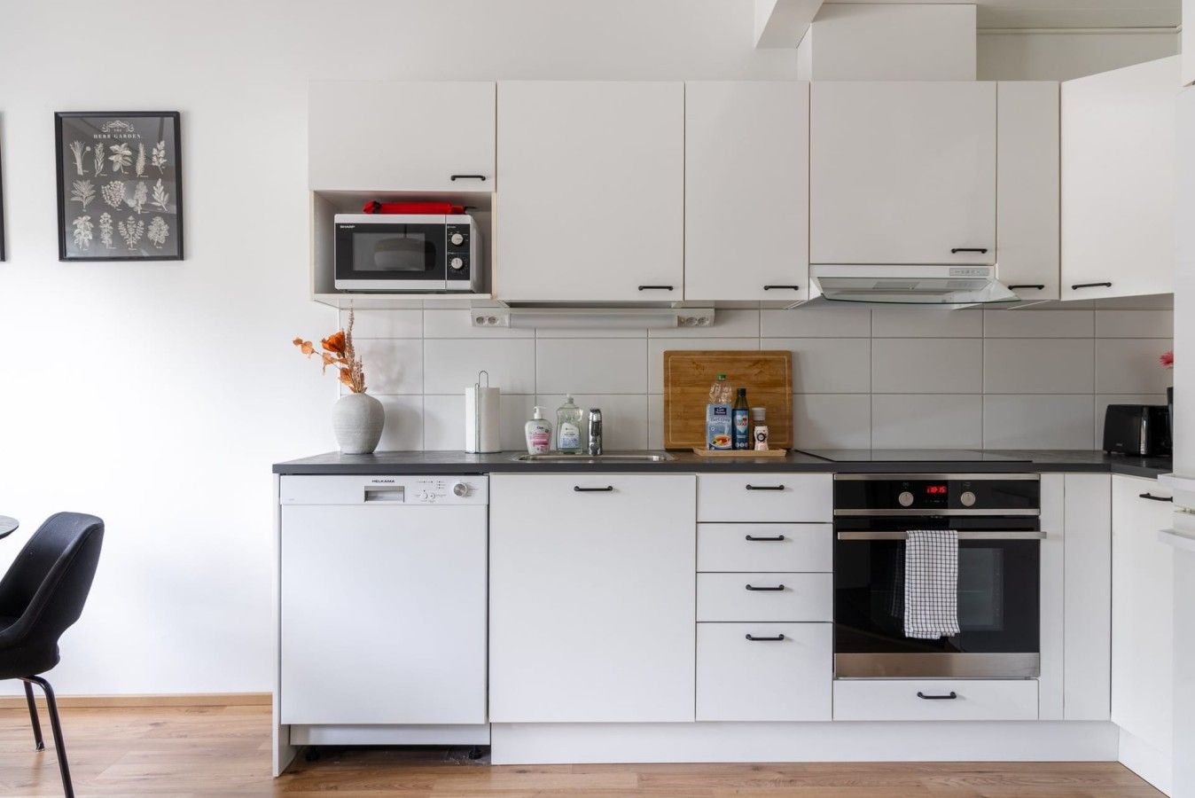 Una cocina moderna con muebles blancos, un microondas, una estufa y un comedor con una silla.