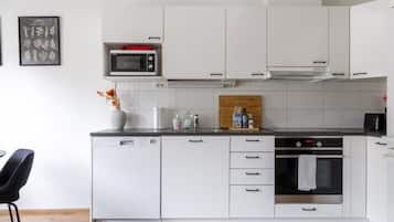 Una cocina moderna con muebles blancos, un microondas, una estufa y un comedor con una silla.