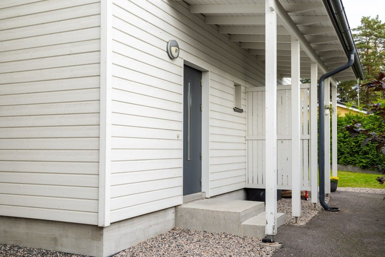 A white building with a dark door, a porch with a railing, and a small step leading to the entrance.
