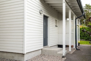 A white building with a dark door, a porch with a railing, and a small step leading to the entrance.