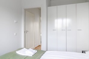 A bedroom with a bed, a green blanket, a white towel, and a white wardrobe.