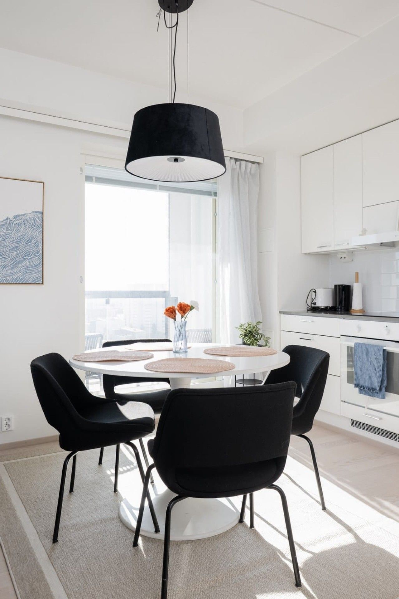 Un'area pranzo moderna con un tavolo rotondo, sedie nere e una lampada a sospensione.