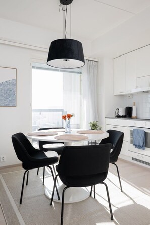 Moderni ruokailutila, jossa on pyöreä pöytä, mustat tuolit ja riippuvalaisin.