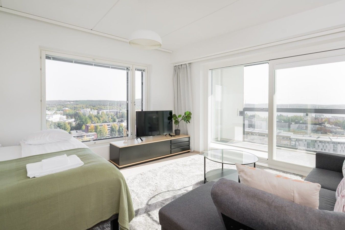 Una camera d'albergo moderna con un letto, un divano, una TV e ampie finestre con vista sulla città.