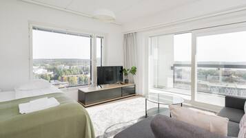 Una camera d'albergo moderna con un letto, un divano, una TV e ampie finestre con vista sulla città.