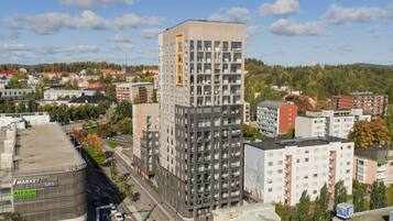 Korkea kerrostalo, jossa on useita kerroksia, ja sen ympärillä on muita rakennuksia ja puita.