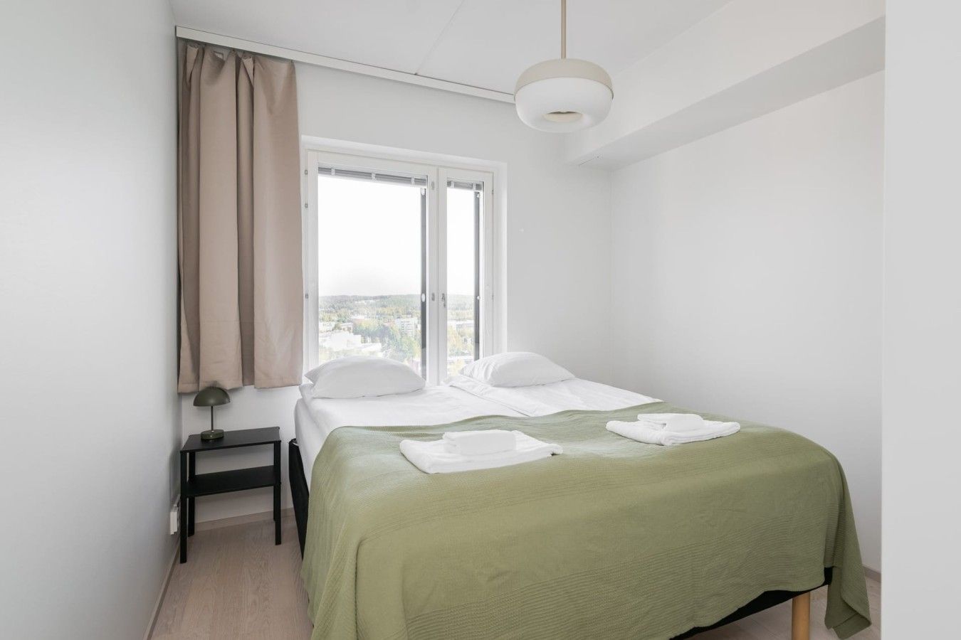 Een minimalistisch ingerichte slaapkamer met een bed, een nachtkastje, een raam met gordijnen en een hanglamp.