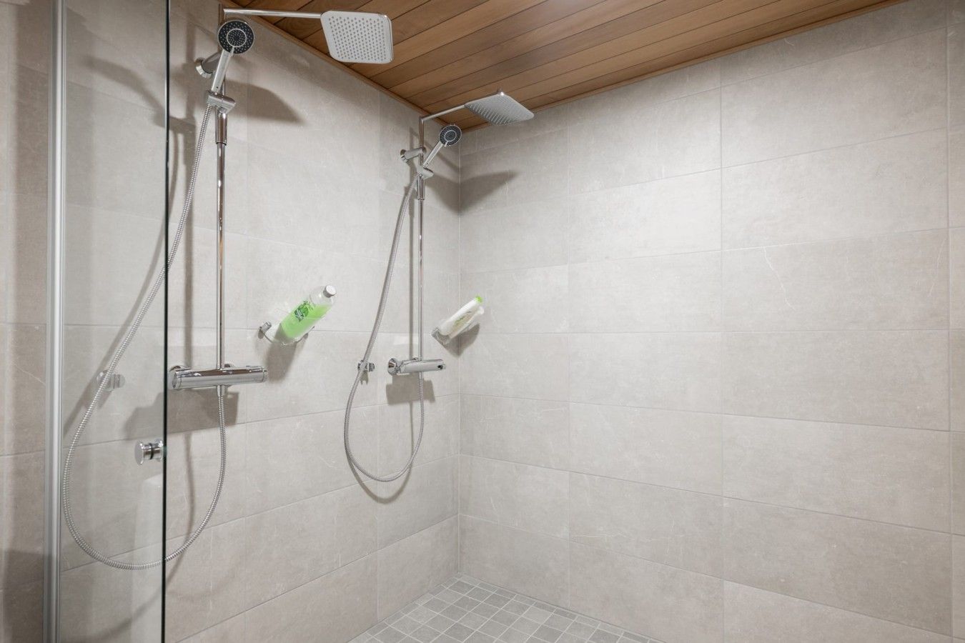 A shower area with a glass door, a wooden ceiling, and tiled walls.