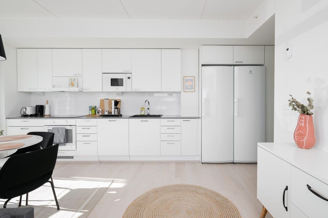 Una cocina moderna con armarios blancos, un refrigerador de dos puertas, un microondas y un lavamanos.