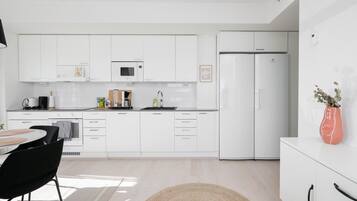 Una cocina moderna con armarios blancos, un refrigerador de dos puertas, un microondas y un lavamanos.