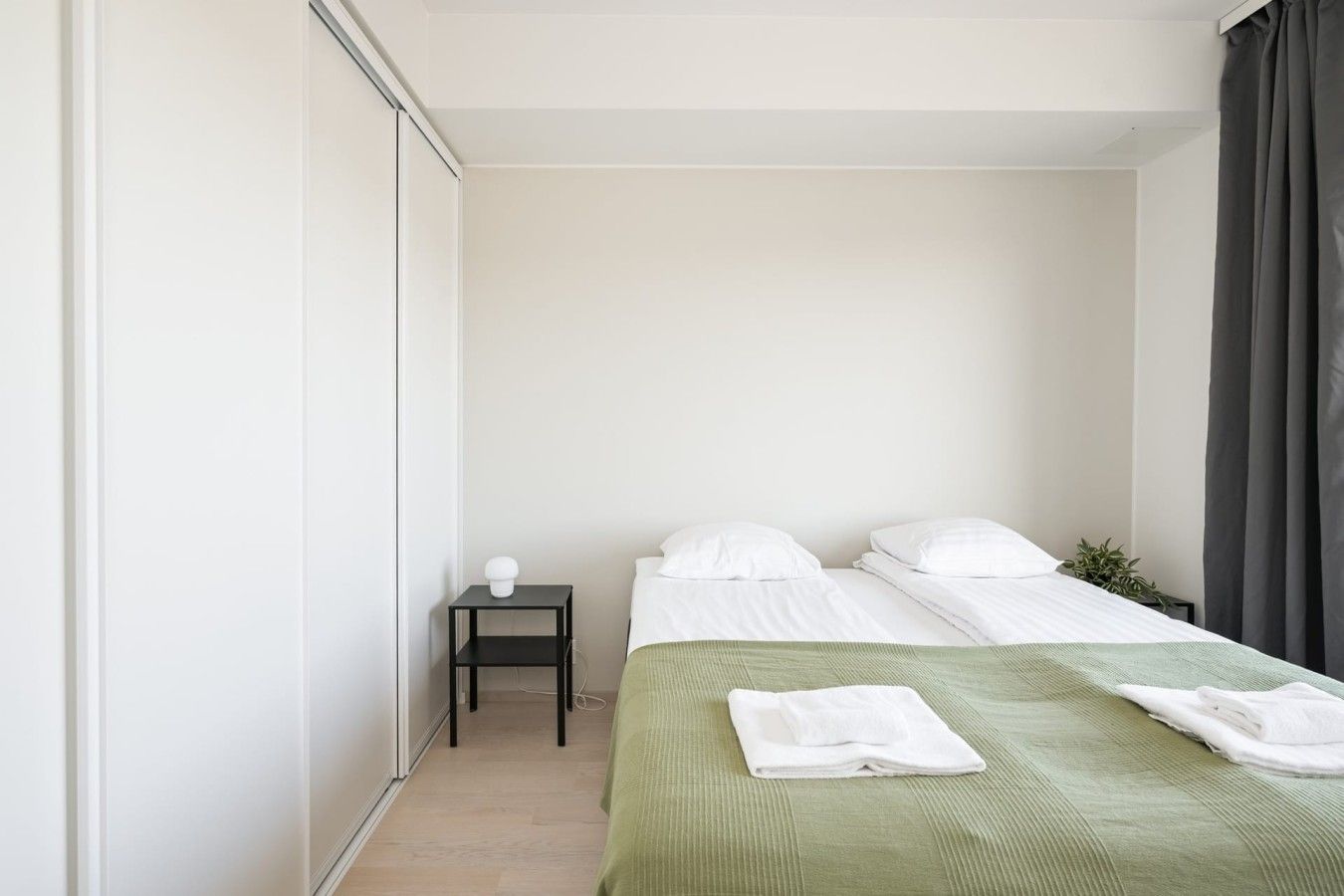 Une petite chambre propre, avec deux lits, une table de chevet et une plante.