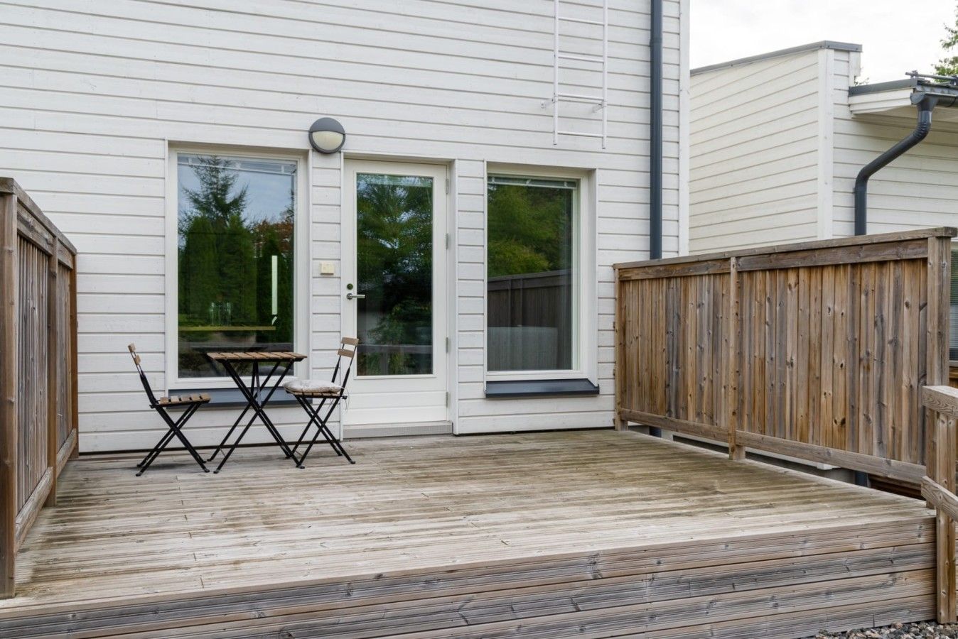 Eine Terrasse mit Tisch und Stühlen, ein Holzzaun und ein Haus mit weißer Außenverkleidung und einer Garagentür.