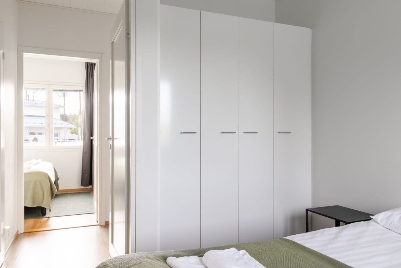 Ein Schlafzimmer mit Bett, Kleiderschrank, kleinem Tisch und Blick ins Freie.