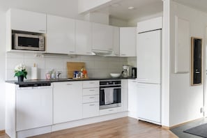 Una cocina moderna con armarios blancos, microondas integrado, cafetera y lavavajillas.