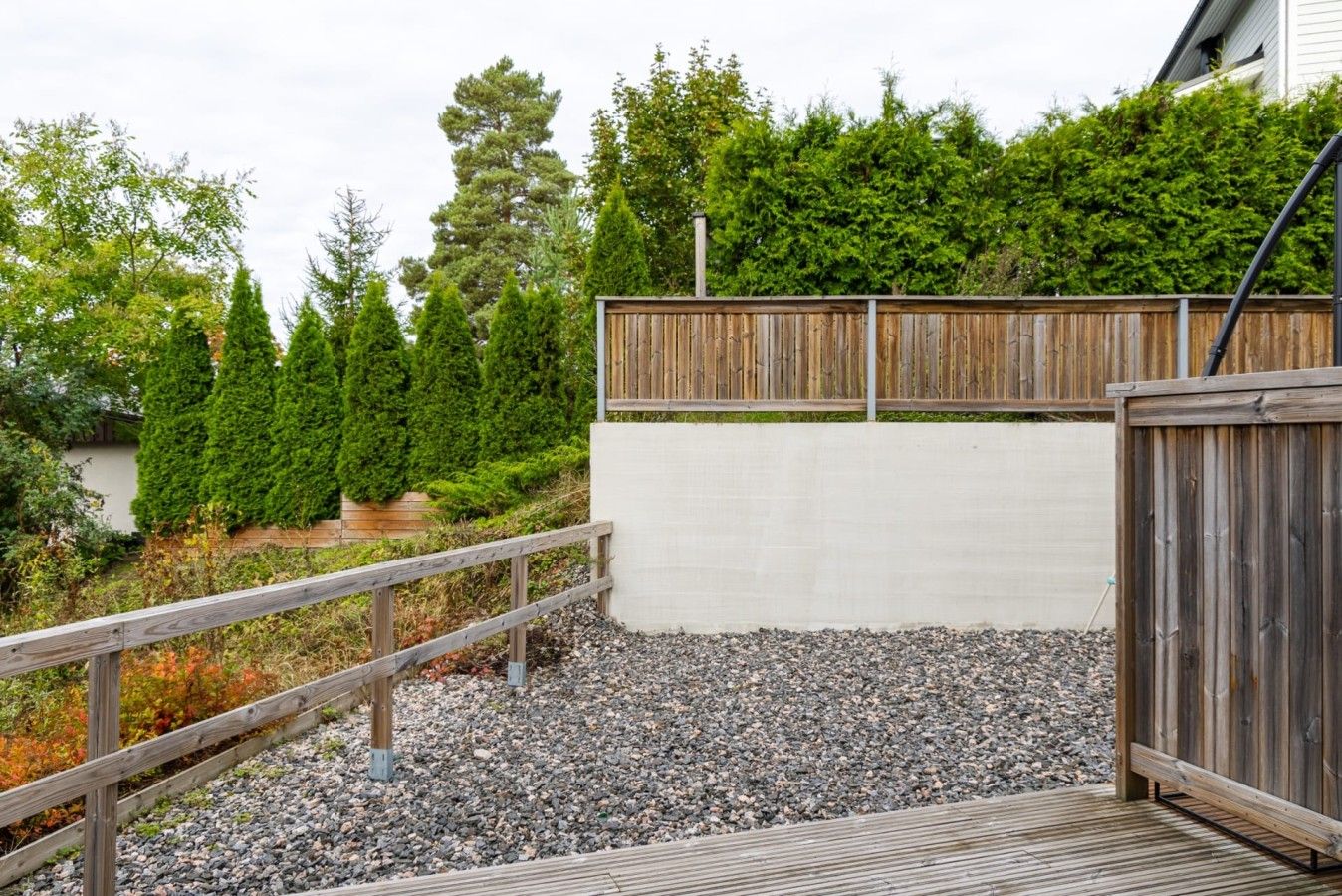 A wooden deck with a metal railing, surrounded by a gravel area and a wooden fence.