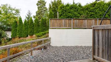 A wooden deck with a metal railing, surrounded by a gravel area and a wooden fence.