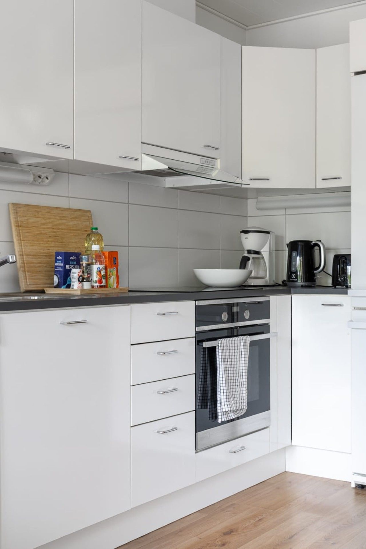 A modern kitchen with white cabinetry, a black countertop, and a stainless steel oven.