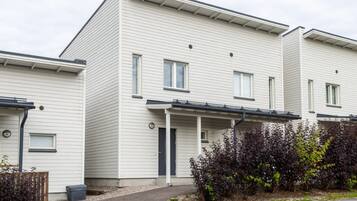 Moderni, kaksikerroksinen asuintalo, jossa on tasakatto, katettu kuisti ja pieni etupiha, jossa on pensaita.