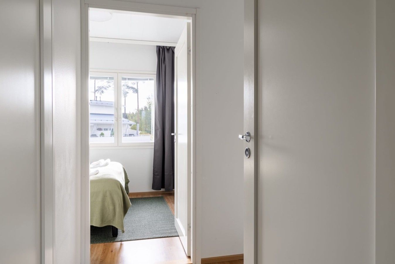 A room with a bed, a window with curtains, and a door.