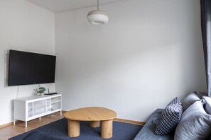 Una sala de estar moderna con un televisor de pantalla plana, una mesa de centro de madera, un mueble blanco para entretenimiento y un sofá gris.