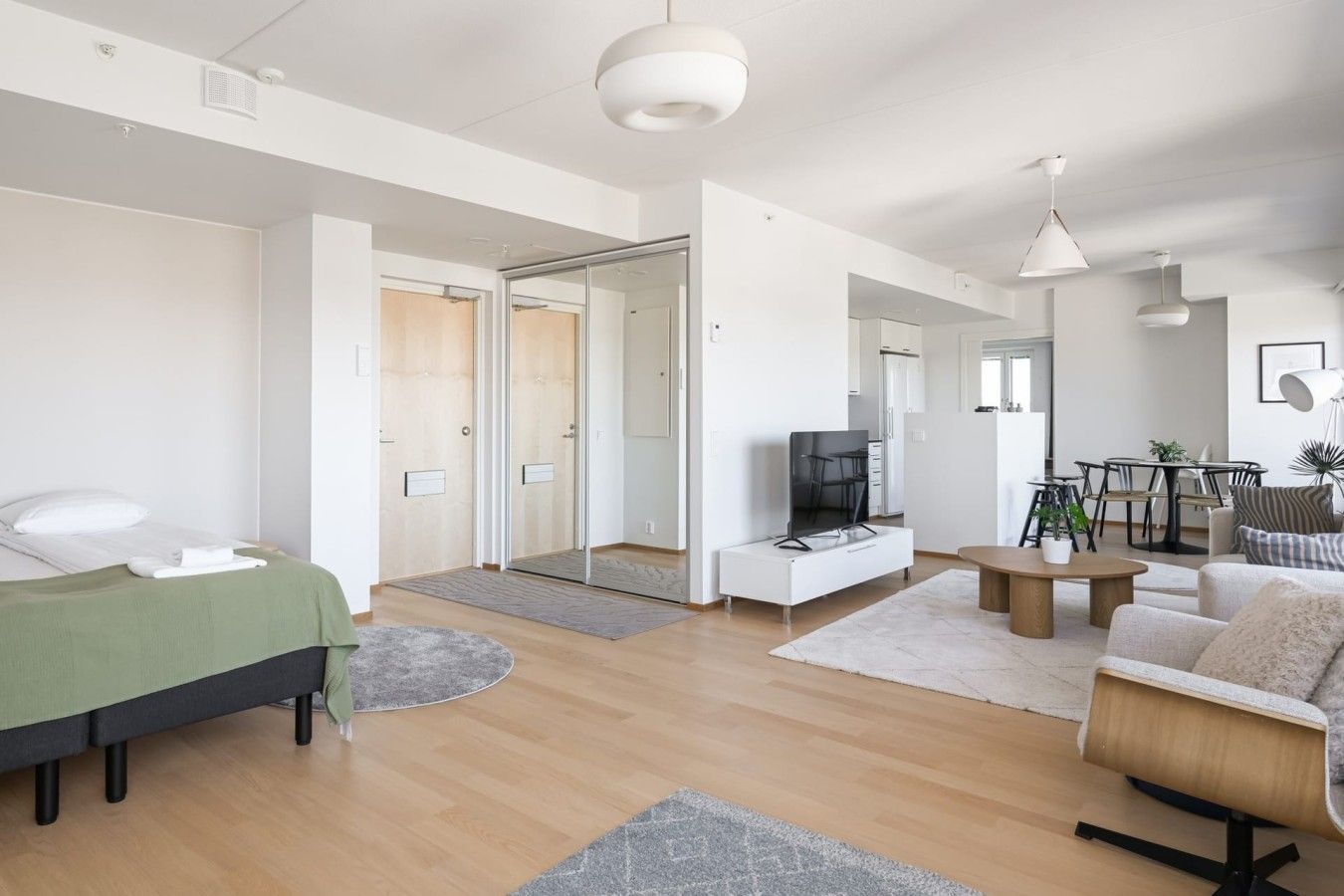 Moderni hotellihuone, jossa on sänky, oleskelualue sohvineen ja sohvapöytineen, televisio sekä ruokailutila tuoleineen ja pöytineen.
