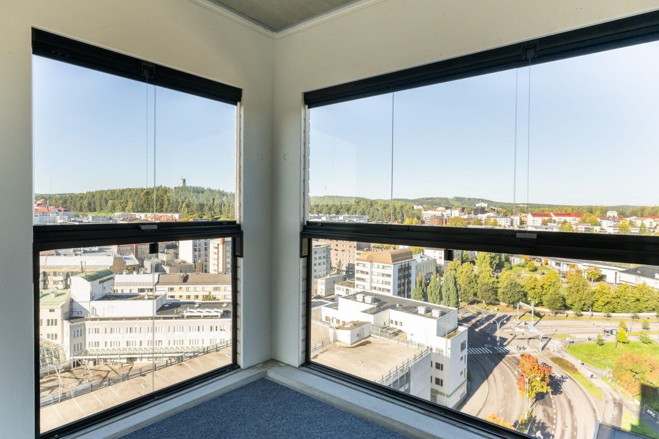 Huoneessa on kaksi suurta ikkunaa, joista avautuu näkymä kaupunkimaisemaan, johon kuuluu rakennuksia ja katu.