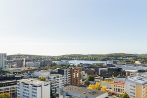 Kaupunkikuva, jossa on moderneja rakennuksia, vesialue ja taustalla metsäinen kukkula.