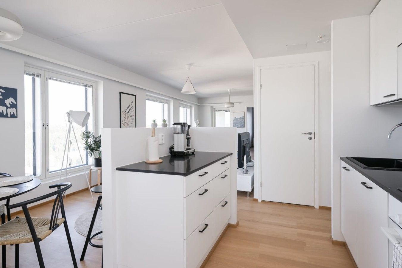 Une cuisine moderne avec des meubles blancs, un plan de travail noir et un coin repas comprenant une table et des chaises.