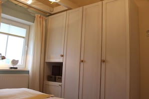 Ein Schlafzimmer mit einem Bett, einem Fenster mit Vorhängen, einem Kleiderschrank und einem Regal mit Körben.