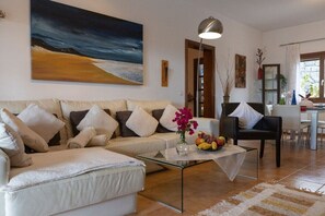 Un salon avec un canapé, une table basse et un tableau représentant une scène de plage.