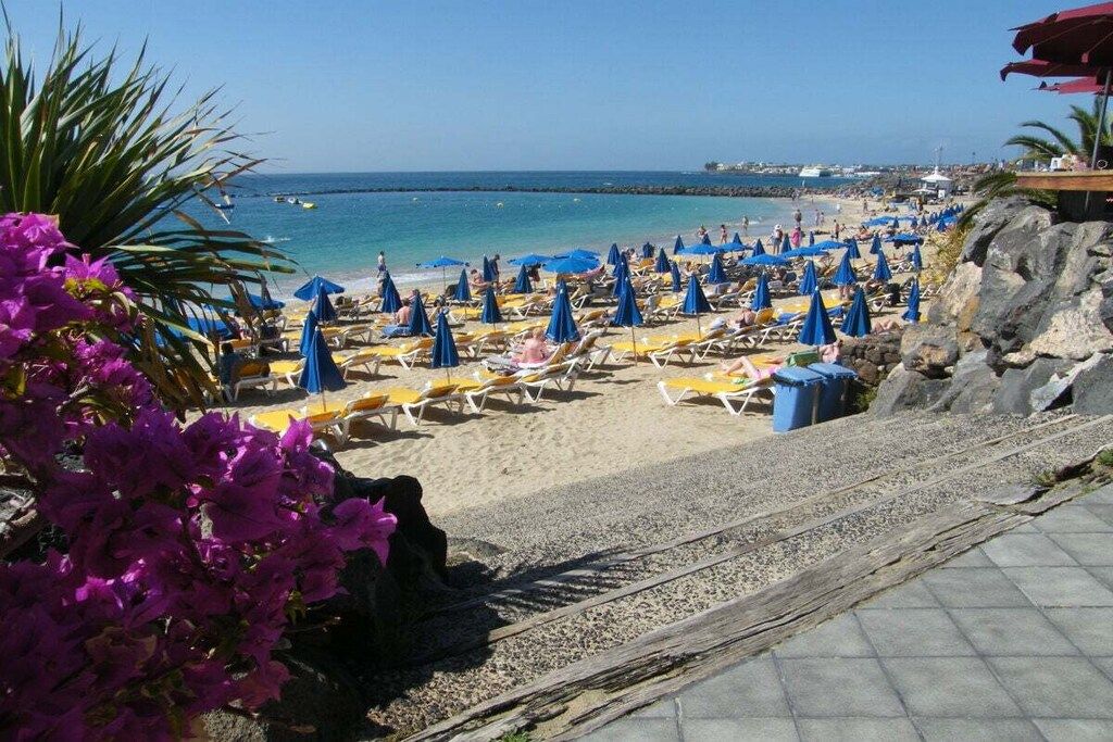 Une plage avec des chaises longues et des parasols, un ciel dégagé et une côte rocheuse.