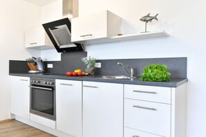 Eine moderne Küche mit weißen Schränken, einem eingebauten Ofen, einer Edelstahl-Spüle und einer kleinen Fischdekoration an der Wand.