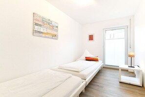 Ein Zimmer mit zwei Einzelbetten, einem Nachttisch mit Lampe, einem Wandbild und einer Tür.