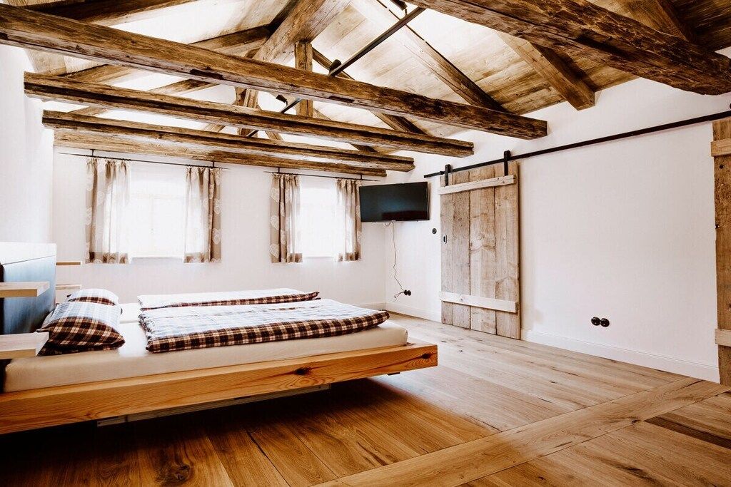 Ein Zimmer mit Holzboden, einem Bett mit Karo-Bettwäsche, einem an der Wand befestigten Fernseher und einer Schiebetür.