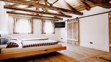 Ein Zimmer mit Holzboden, einem Bett mit Karo-Bettwäsche, einem an der Wand befestigten Fernseher und einer Schiebetür.