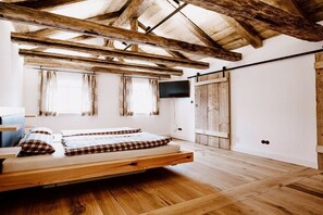 A room with a wooden ceiling, a bed with plaid bedding, a television on the wall, and a sliding door. - Jura Chalet Eggersberg (Obereggersberg)