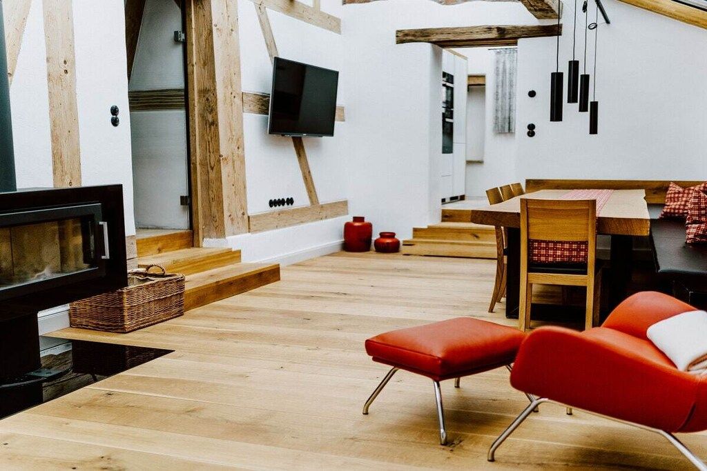 Ein modernes Interieur mit einem an einer weißen Wand befestigten Flachbildfernseher, Holzböden, einem Essbereich mit Tisch und Stühlen sowie einer roten gepolsterten Bank.