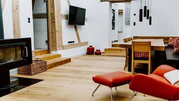 Ein modernes Interieur mit einem an einer weißen Wand befestigten Flachbildfernseher, Holzböden, einem Essbereich mit Tisch und Stühlen sowie einer roten gepolsterten Bank.